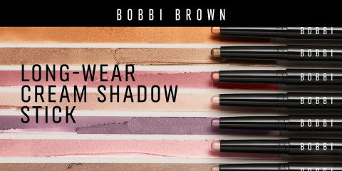Una selección de lápices de sombra de ojos en crema de larga duración de Bobbi Brown en varios tonos, presentados horizontalmente sobre una superficie texturizada. Cada lápiz está abierto, revelando los colores cremosos. El nombre de la marca es visible en las tapas.