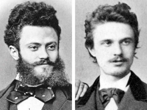 Zwei Männer in formeller Kleidung aus dem 19. Jahrhundert und mit Fliege. Der Mann links hat einen Vollbart und lockiges Haar, während der Mann rechts einen Schnurrbart und welliges Haar hat. Auf den sepiafarbenen Porträts scheinen beide von der Kamera wegzuschauen.