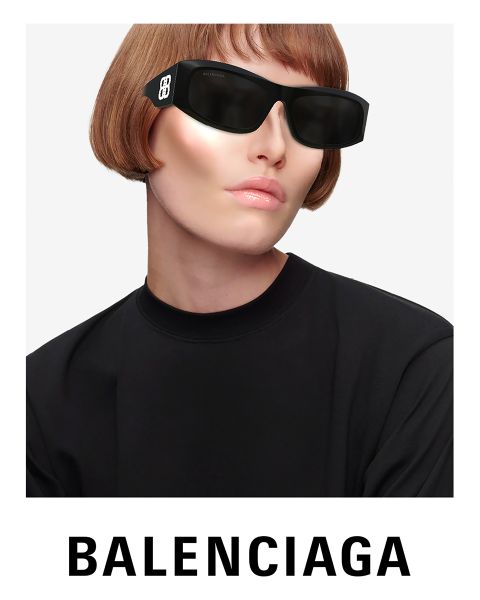 Una persona con gafas de sol negras futuristas y una parte superior negra posa frente a un fondo brillante. Lleva un corte bob corto de color marrón claro. En la parte inferior se puede ver claramente el logotipo de Balenciaga.