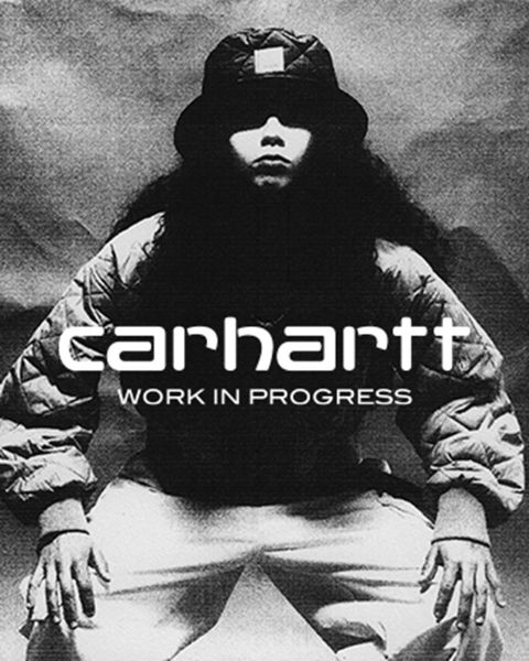 Imagen en blanco y negro de una persona con sombrero y chaqueta, agachada con las manos sobre las rodillas. El texto "Carhartt Work In Progress" se ve prominentemente en el centro.
