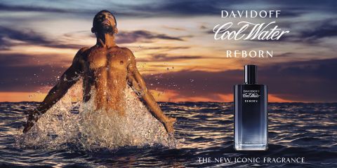 Un hombre sin camisa emerge del mar con los brazos extendidos. El cielo está en tonos naranja y púrpura, lo que sugiere un atardecer o un amanecer. En primer plano, se ve una botella de perfume Davidoff Cool Water Reborn. El texto dice "La nueva fragancia de culto".