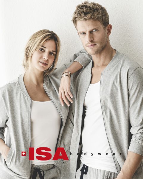 Una mujer y un hombre están de pie uno al lado del otro. Ambos llevan sudaderas grises a juego sobre camisetas blancas y pantalones grises. La mujer tiene su mano en el hombro del hombre. En la parte inferior de la imagen se ve el logo de "ISA Bodywear".