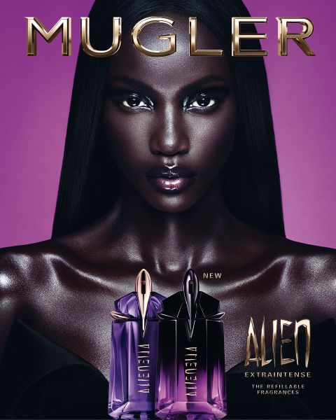Una mujer con una piel oscura y radiante y un cabello negro liso posa delante de un fondo violeta. Delante de ella hay dos frascos de perfume Alien de Mugler. El texto dice "MUGLER" y "ALIEN EXTRA INTENSE LAS FRAGANCIAS RECARGABLES".