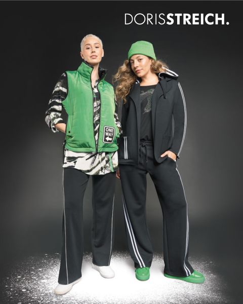 Dos mujeres posan con confianza con atuendos en blanco y negro con toques verdes, incluyendo un chaleco acolchado, un gorro y zapatos, frente a un fondo oscuro con el texto "DORIS STREICH" encima de ellas.