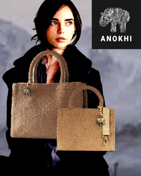 En el fondo, se ve a una mujer con el pelo corto y oscuro. En primer plano, hay dos bolsos marrones texturizados con colgantes de elefantes, y en la esquina superior derecha aparece un logotipo de "ANOKHI" con un elefante estilizado.