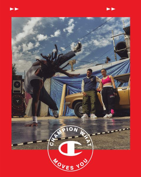 Un breakdancer realiza un headspin en una colchoneta al aire libre, mientras un hombre y una mujer observan. Están de pie junto a un coche antiguo frente a un paisaje urbano con lonas azules y un cielo nublado. Un marco rojo con el texto y el logotipo "Champion Lo Que Te Mueve" rodea la imagen.