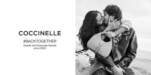 Una fotografía en blanco y negro muestra a una pareja sonriendo y abrazándose en una playa rocosa. El hombre sostiene un bolso. El texto a la izquierda dice: "Coccinelle #BACKTOGETHER Alessio y Emanuela están comprometidos desde 2020".