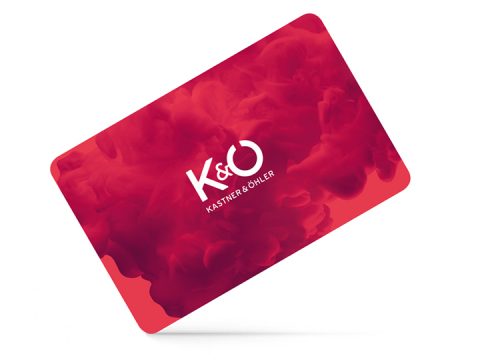 Una tarjeta de regalo roja con las letras blancas "K&O" y debajo la inscripción "KASTNER & ÖHLER". El fondo está adornado con un patrón arremolinado de humo rojo.