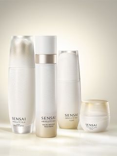 Cuatro elegantes productos blancos para el cuidado de la piel Sensai Absolute Silk, que incluyen botellas y un frasco, están dispuestos con una luz suave y brillante.