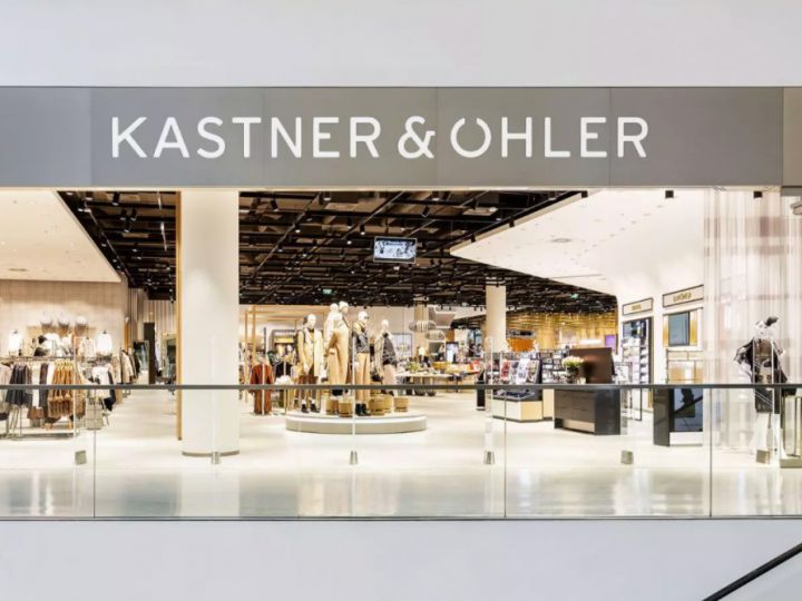 La fachada de la tienda Kastner & Öhler muestra un interior de grandes almacenes moderno con maniquíes que exhiben ropa. El nombre de la tienda se ve claramente en un letrero limpio y moderno sobre la entrada.
