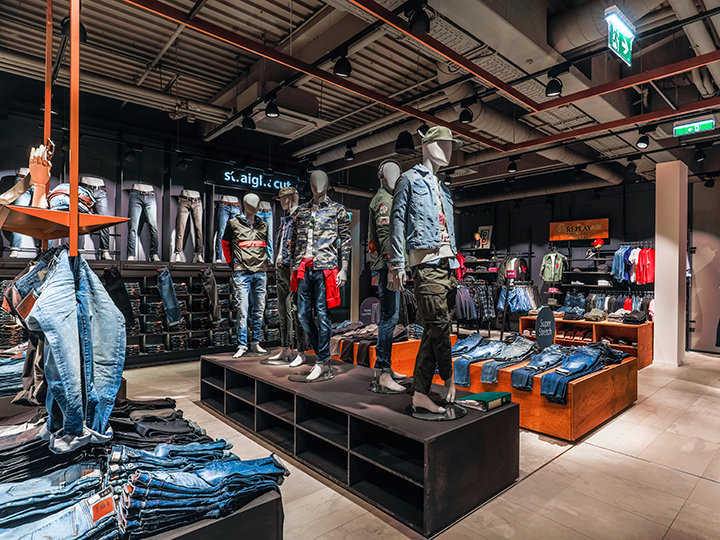 Una tienda de ropa moderna con maniquíes vestidos con ropa informal, que incluye jeans y chaquetas. Estantes y perchas exhiben una variedad de prendas de mezclilla bajo una iluminación brillante, creando un ambiente moderno y elegante.