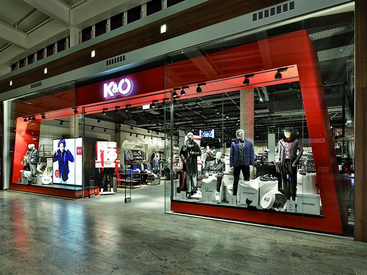 Escaparate de K&Ö en un centro comercial con maniquíes en varios estilos de ropa. La exhibición incluye chaquetas, camisas y accesorios bajo una iluminación brillante, y se pueden ver más prendas en el interior.