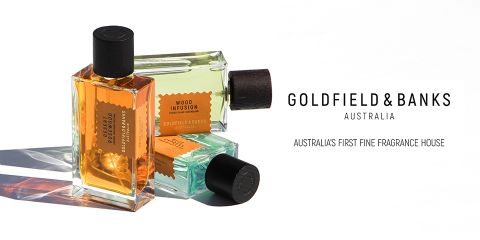 Se muestran tres frascos de perfume de Goldfield & Banks con tapas oscuras y recipientes de vidrio rectangulares llenos de líquidos de diferentes colores. El texto dice "Goldfield & Banks Australia" con el lema "La primera casa de perfumes de Australia".