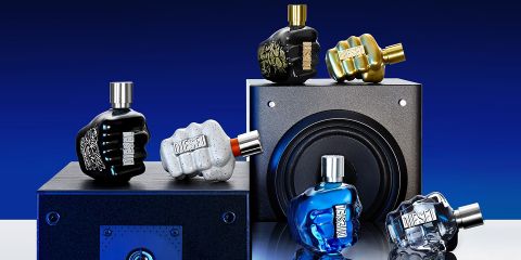 Se muestran varias botellas de perfume con forma de puños cerrados sobre y alrededor de un altavoz negro frente a un fondo degradado azul. Las botellas vienen en varios colores, incluyendo negro, dorado, gris, azul y transparente.