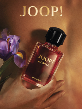 Una botella de JOOP! Homme Le Parfum se sostiene frente a un fondo borroso con una flor de iris violeta. El logo dorado de "JOOP!" es claramente visible en la parte superior. La imagen transmite elegancia y lujo.