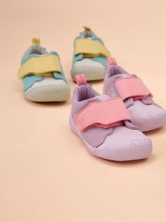 Dos pares de zapatos de niño sobre un fondo beige: un par es de color lavanda claro con tiras rosas, el otro es de color azul claro con tiras amarillas.