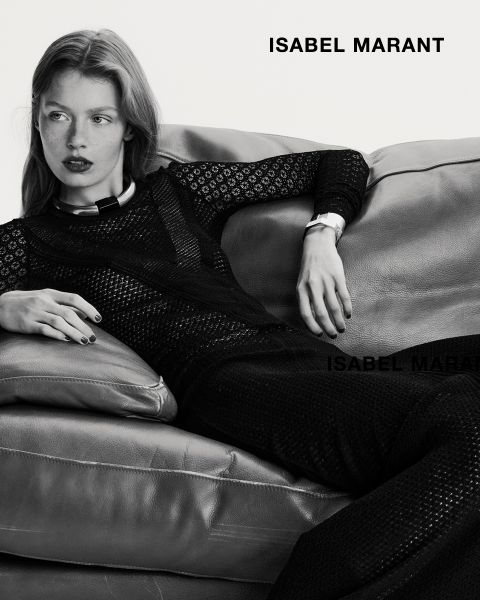 Una mujer está recostada en un sofá de cuero, vestida con un conjunto negro texturizado de manga larga. La imagen está en blanco y negro, con la inscripción "ISABEL MARANT" en negrita en las esquinas superior derecha e inferior.
