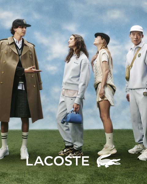Cuatro modelos posan al aire libre con atuendos de Lacoste frente a un cielo azul. De izquierda a derecha: una persona con gabardina, una persona con suéter y pantalones, una persona con chaleco y falda y una persona con un chándal. El logo de Lacoste está en la parte inferior.