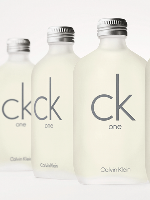 Se ven cuatro frascos esmerilados de Calvin Klein CK One frente a un fondo claro. Los frascos llevan la inscripción gris "ck one" y cierres plateados.
