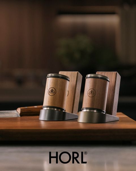 Dos afiladores de cuchillos de madera y metal, así como un soporte para cuchillos de madera sobre una base de madera, con el logo "HORL" en la parte inferior.