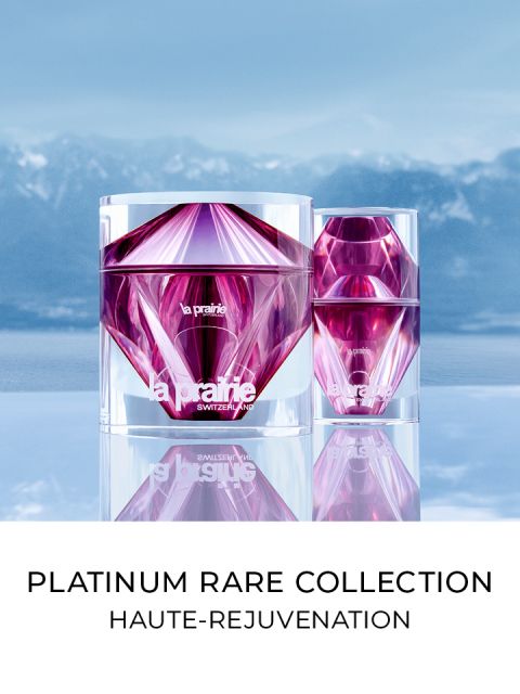 Dos lujosos recipientes facetados en tonos rosa y violeta se alzan sobre un fondo de cielo azul y montañas. Debajo de los recipientes se lee el texto "Platinum Rare Collection Haute-Rejuvenation".