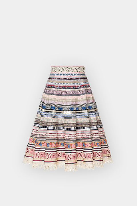 Una falda hasta la rodilla con línea A, con rayas horizontales de colores, patrones intrincados y bordados de flores sobre un fondo blanco.