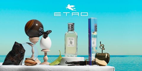 Frasco de perfume con la inscripción "ETRO" y un diseño de piña, rodeado de decoración artística: una esfera, un huevo con una mariposa, una piedra, una hoja, nueces, una manzana dorada y una mano moldeada. En la parte superior, el logotipo de ETRO sobre un fondo de cielo azul y mar.
