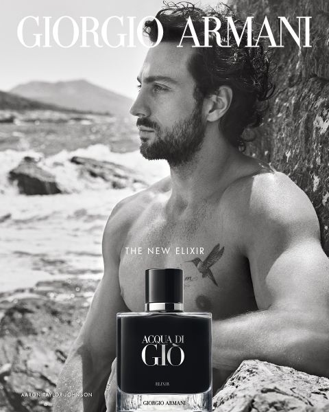 El anuncio en blanco y negro de Acqua di Giò Elixir de Giorgio Armani muestra a un hombre con el torso desnudo y cabello rizado sentado en unos acantilados rocosos junto al mar, mirando a la distancia. En primer plano se puede ver el frasco de la fragancia.