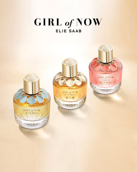 Tres frascos de perfume "Girl of Now" de Elie Saab se presentan sobre una superficie de oro claro, cada uno con una combinación de colores única: acentos azules, dorados y rosas. Los tapones son dorados y el nombre de la marca con el título de la colección aparece encima de los frascos.