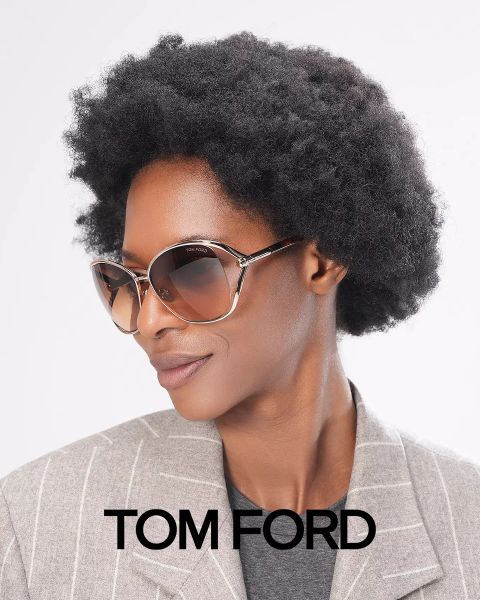 Persona con un peinado afro corto, que lleva gafas de sol grandes y una chaqueta gris a rayas. En la imagen aparece abajo "Tom Ford". El fondo es blanco liso.
