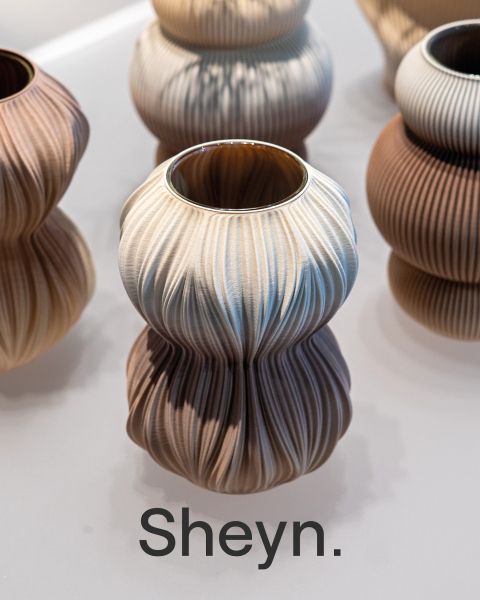 Un jarrón escultórico de cerámica con textura ondulada en tonos neutros, que incluye las letras en negrita Sheyn".