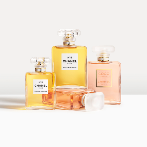 Cuatro frascos de perfume de Chanel, incluyendo dos No. 5 Eau de Parfum con líquido dorado y dos Coco Mademoiselle, están dispuestos sobre una superficie blanca. Los perfumes están en elegantes frascos de vidrio con tapones cuadrados que proyectan sombras suaves.