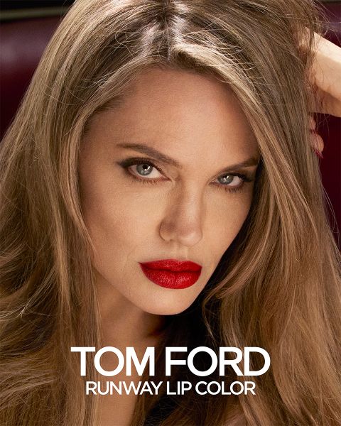 Una persona con cabello largo y lápiz labial rojo brillante mira atentamente. La imagen es un anuncio de Tom Ford Runway Lip Color, con el nombre del producto mostrado en letras blancas en la parte inferior.