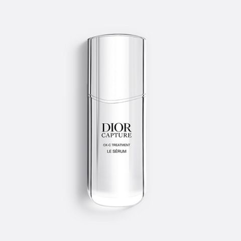 Un frasco delgado y translúcido de Dior Capture OX-C Treatment Le Sérum. El frasco es alto y curvo, con un diseño minimalista y texto negro en el frente. Sobre un fondo gris claro.
