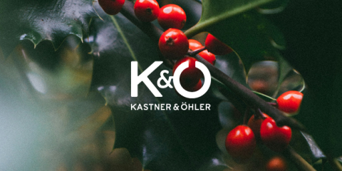 Eine Nahaufnahme glänzender grüner Blätter mit Trauben leuchtend roter Beeren. Im Vordergrund steht der Text „K&O“ und darunter in Weiß „Kastner & Öhler“, das das Bild überlagert.