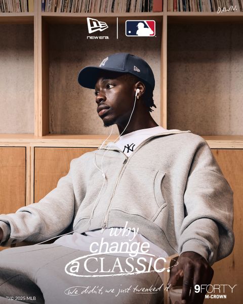 Un hombre con un chándal gris, una camiseta blanca y una gorra azul marino de los New York Yankees está sentado en un banco de madera escuchando música con auriculares blancos. El texto promociona la gorra 9FORTY M-Crown de New Era con la marca MLB.