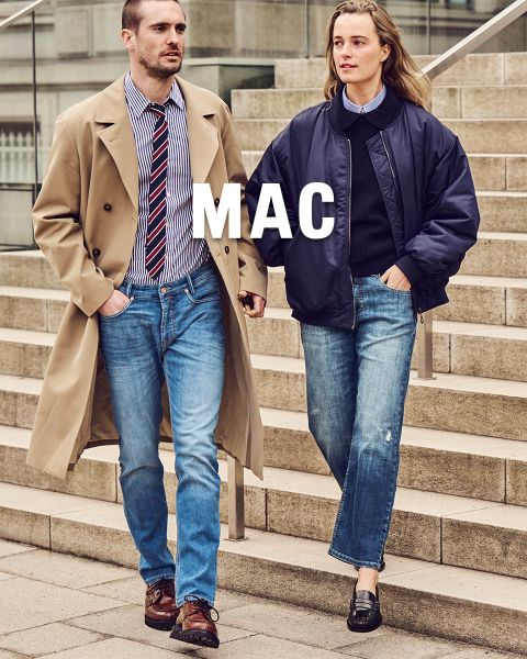 Un hombre con gabardina y una mujer con chaqueta azul marino bajan unas escaleras de piedra en vaqueros. Encima de la imagen se ve la inscripción "MAC".