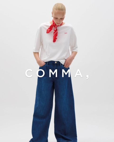 Una mujer con un abrigo a cuadros y accesorios dorados posa con un perro marrón claro y blanco con un atuendo a cuadros a juego. La palabra "COMMA" aparece en letras blancas grandes a través de la imagen.