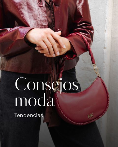 Una persona con una brillante chaqueta de cuero color burdeos sostiene un bolso de mano color burdeos a juego con el logo de MK. El texto en la imagen dice: "Consejos moda. Tendencias 2025.