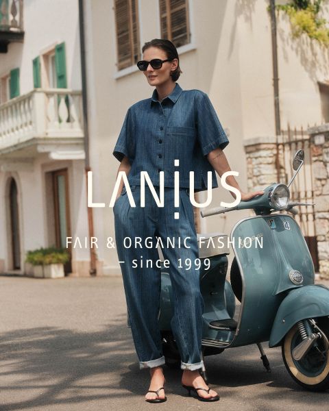 Una mujer con un vestido largo azul oscuro está sentada entre formaciones rocosas en capas. El texto superpuesto dice: "LANIUS FAIR & ORGANIC FASHION - desde 1999.