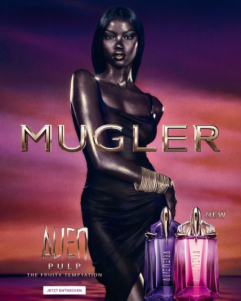 Una mujer con una piel oscura y radiante y un cabello negro liso posa delante de un fondo violeta. Delante de ella hay dos frascos de perfume Alien de Mugler. El texto dice "MUGLER" y "ALIEN EXTRA INTENSE LAS FRAGANCIAS RECARGABLES".