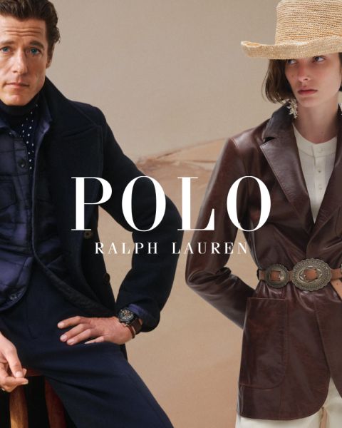 Un hombre y una mujer visten elegantes gabardinas de Ralph Lauren. El hombre combina su abrigo con un jersey colorido y pantalones grises, mientras que la mujer lleva una camisa a rayas, guantes marrones y un cinturón ancho. "POLO RALPH LAUREN" se muestra en letras blancas.