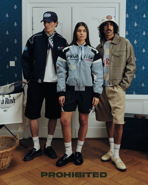 Dos hombres están sentados en una plataforma de madera en la hierba alta jugando al backgammon. Uno lleva un gorro rojo, una camisa a cuadros y vaqueros, el otro lleva un gorro marrón rojizo, una chaqueta verde oliva y pantalones oscuros. Encima de ellos está escrito "PROHIBIDO".