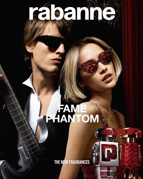 Dos frascos del perfume Rabanne Olympéa ABSOLU, uno negro y otro rosa, se exhiben frente a una flor blanca floreciente sobre un fondo oscuro. El texto dice: "Rabanne OLYMPÉA ABSOLU - LA NUEVA FRAGANCIA".