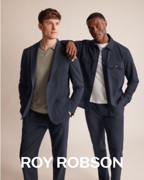 Un hombre está de pie al aire libre frente a montañas nevadas y lleva un abrigo de pata de gallo gris, un jersey gris y pantalones grises. El texto "ROY ROBSON" aparece en la parte inferior de la imagen.