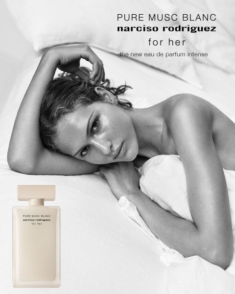 Una mujer con cabello castaño rizado posa de perfil junto a un frasco de perfume rosa que dice "all of me narciso rodriguez floral". El texto de arriba dice "narciso rodriguez", y debajo: "El nuevo Eau de Parfum floral".