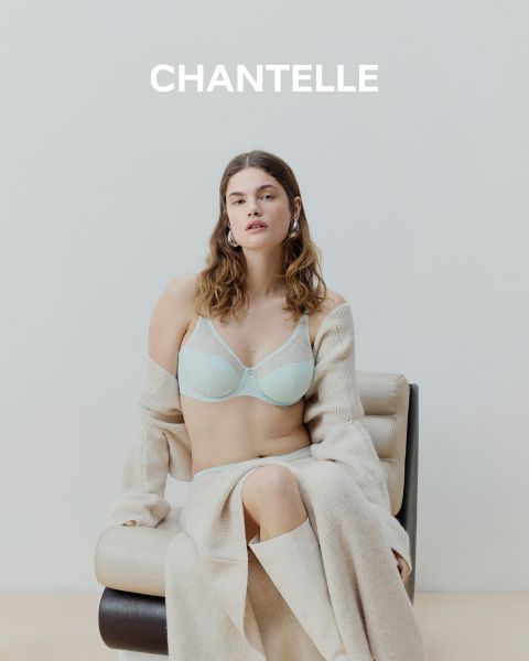 Una mujer con un vestido lencero negro de encaje y gafas de sol sentada en un barco cerca de un río urbano, con edificios y árboles al fondo. La palabra "CHANTELLE" se puede leer en la parte inferior de la imagen.