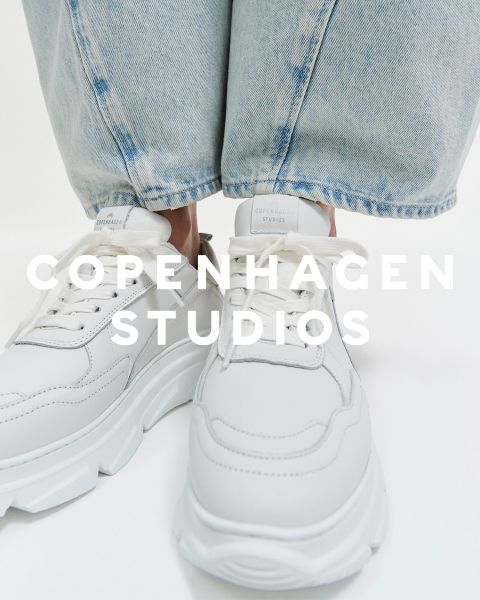 Primer plano de zapatillas blancas con suelas gruesas que lleva una persona con vaqueros azul claro. El texto "COPENHAGEN STUDIOS" está superpuesto en la imagen.
