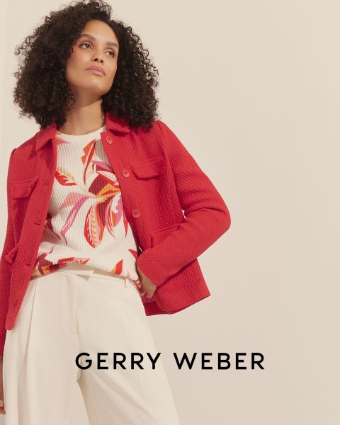 Una mujer con cabello rizado lleva una chaqueta roja texturizada sobre una blusa floral colorida y pantalones color crema. El fondo es sencillo y en la parte inferior se ve el texto "Gerry Weber".