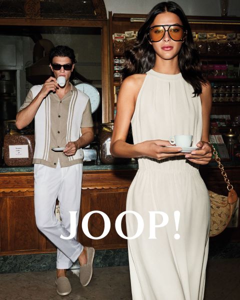 Hombre y mujer con ropa de verano elegante en un café. El hombre lleva una camisa beige y sostiene una taza, mientras que la mujer con un vestido claro sostiene un platillo. Ambos llevan gafas de sol. "JOOP!" se ve claramente.